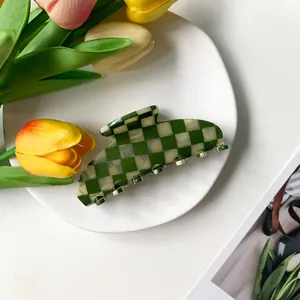 Large green checkered acetate hair claw clip on a white ceramic plate with tulips