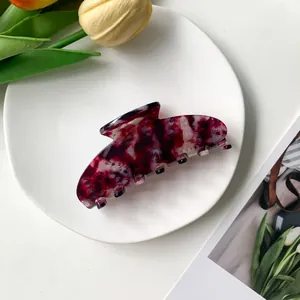 Detail of a large acetate claw clip with red marble texture on a white ceramic plate