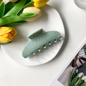 Blue checkerboard acetate hair claw clip displayed on a white plate with yellow tulips