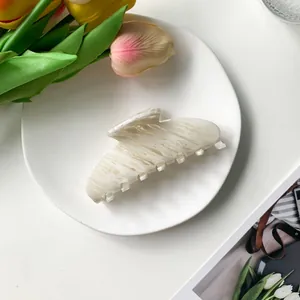 Detail of a beige acetate hair claw clip with marble texture on a ceramic plate