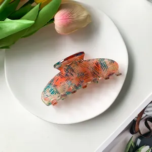 Detailed top view of a large translucent coral orange hair claw clip on a minimalist plate
