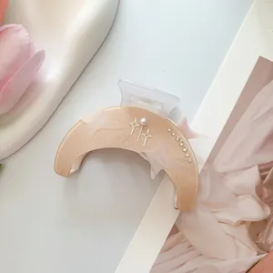Detalle de pinza para el pelo de luna con estrellas y perla sobre resina beige mate