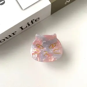 Detail of pink marble acetate cat hair claw clip with golden eyes on a book