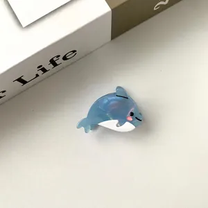 Gros plan d'une mini pince à cheveux dauphin bleue pailletée en acétate sur un livre