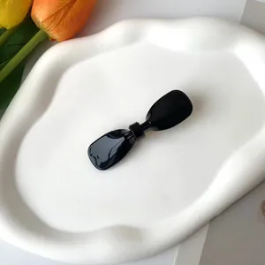 Eleganter schwarzer Acetat-Haarclip in Schleifenform auf weißem Keramiktablett