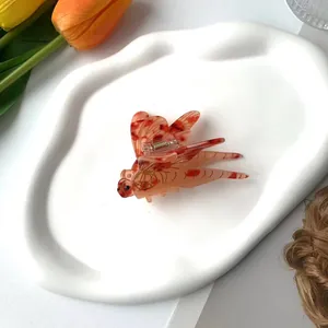 Pince à cheveux libellule en acétate avec texture ambre sur un plateau blanc élégant