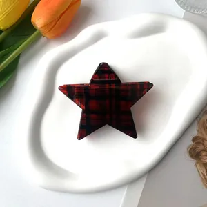 Star-shaped hair claw clip with red and black plaid pattern on a ceramic dish