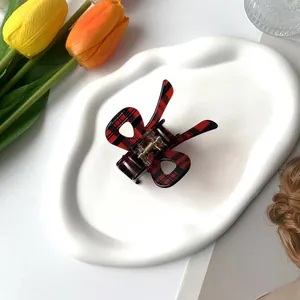 Close-up of a red and black plaid butterfly hair claw clip on a white decorative tray