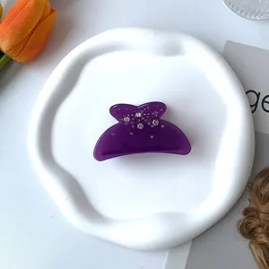 Détail d'une pince à cheveux violette translucide avec strass sur un plateau déco