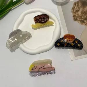 Creative acetate hair clips in snail, moon, and star designs on a ceramic tray