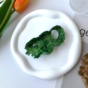 Green acetate dragon hair claw clip with gold lines on a white ceramic plate