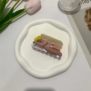Close-up of artistic goddess shaped acetate hair claw clip on a ceramic tray with flowers