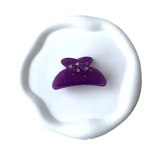 Pince à cheveux noeud en acrylique violet avec strass scintillants sur plateau blanc