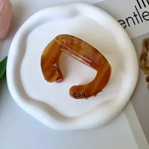 Detail of amber tortoiseshell claw clip with Can lettering on white ceramic plate