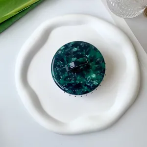 Top view of circular acetate scalp massager with green marble texture on a white tray