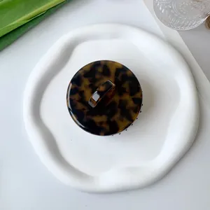 Top view of a round tortoiseshell resin hair claw clip on a white decorative ceramic plate