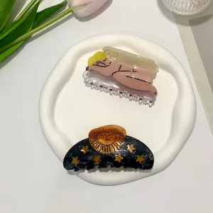 Artistic acetate hair claws with angel and moon sun motifs in a decorative ceramic dish