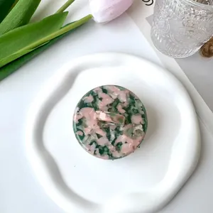 Detail view of round acetate hair claw with green and pink marble texture on ceramic plate