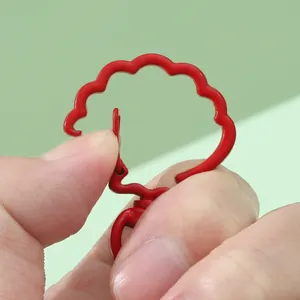 Red candy-colored shell-shaped lacquer keychain hook being opened in a close-up hand shot