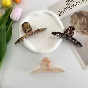 Three long acetate hair claws with marble and tortoiseshell patterns on ceramic tray