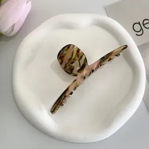 Artistic marble textured acetate hair claw clip displayed on a white tray with tulip