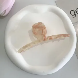 Macro view of peach marble acetate hair claw clip on a white decorative ceramic tray