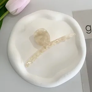 Detailed close-up of a large cream acetate hair claw clip with marble texture on a tray