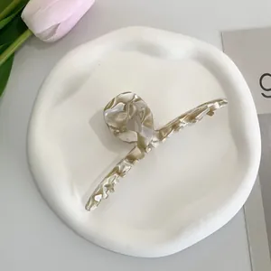 Close-up of white and brown tortoiseshell acetate hair claw clip on a minimalist tray