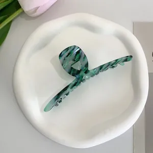 Detailed macro of dark green marble acetate hair claw clip on a ceramic tray display