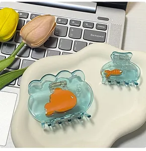 Detail of two goldfish-shaped hair clips in blue acrylic on a white decorative tray