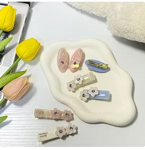 Dettaglio di sette fermagli per capelli a fiore in acetato con cristalli su vassoio bianco