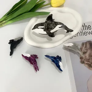 Set of whale-shaped acetate hair claws in various marble textures on a white ceramic tray