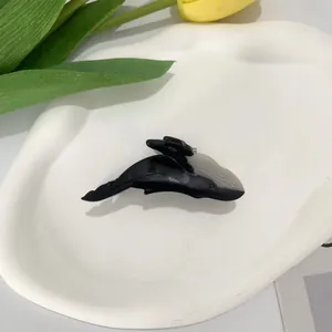 Cute orca-shaped acetate hair claw clip in black and grey, placed on a ceramic tray