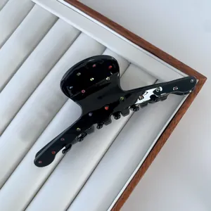 Close-up of black acetate hair claw clip with colorful rhinestones on a display tray