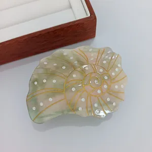 Détail d'une pince à cheveux coquillage avec spirales dorées et texture en acétate