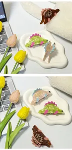 Dettaglio di mini mollette per capelli a forma di dinosauro in acetato dai colori vivaci