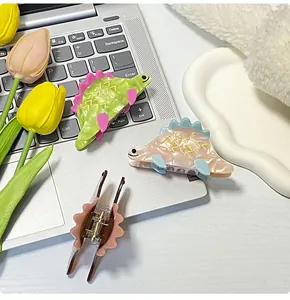 Dettaglio delle mollette a dinosauro nei colori verde e rosa pastello su laptop