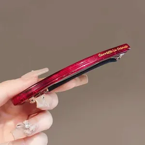 Détail de barrette en acétate rouge pailleté avec lettrage doré sur clip métallique