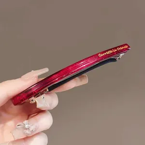 Barrette en résine rouge translucide avec lettrage doré et pince en métal doré