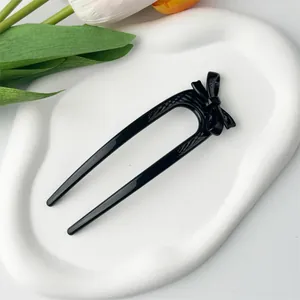 Detail of a sleek black U-shaped hair pin featuring a glossy resin bow decoration