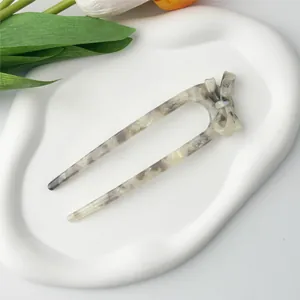 Detail of marble pattern acetate U-shaped hair fork with bow on ceramic tray