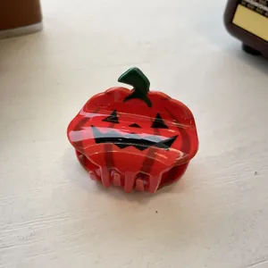 Detailed close-up of a pumpkin-shaped Halloween hair claw clip on a white wood surface