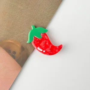 Détail macro d'une pince à cheveux en acétate en forme de piment rouge avec tige verte