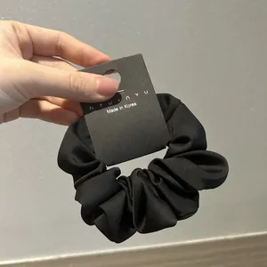 Detalle de un coletero de satén negro con pliegues suaves y etiqueta de marca en mano
