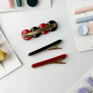 Red and black resin hair clips with golden metal base on a white flat lay background