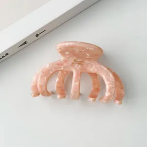 Detailansicht der Haarspange aus Acetat in Rosa-Marmor mit goldenem Logo und Zähnen