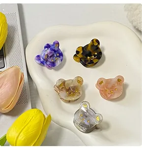 Fünf bunte Mini-Haarklammern aus Acetat in Bärenform mit Marmortextur auf einer Schale