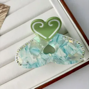 Detailed view of heart-shaped hair claw with green acetate and sparkling rhinestones