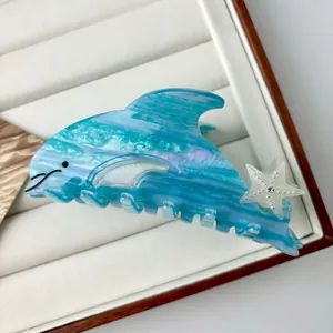 Blue seashell dolphin hair claw clip with star detail on white jewelry tray