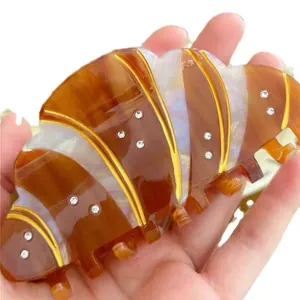 Detailed view of croissant hair claw clip with rhinestones and gold edges held in hand